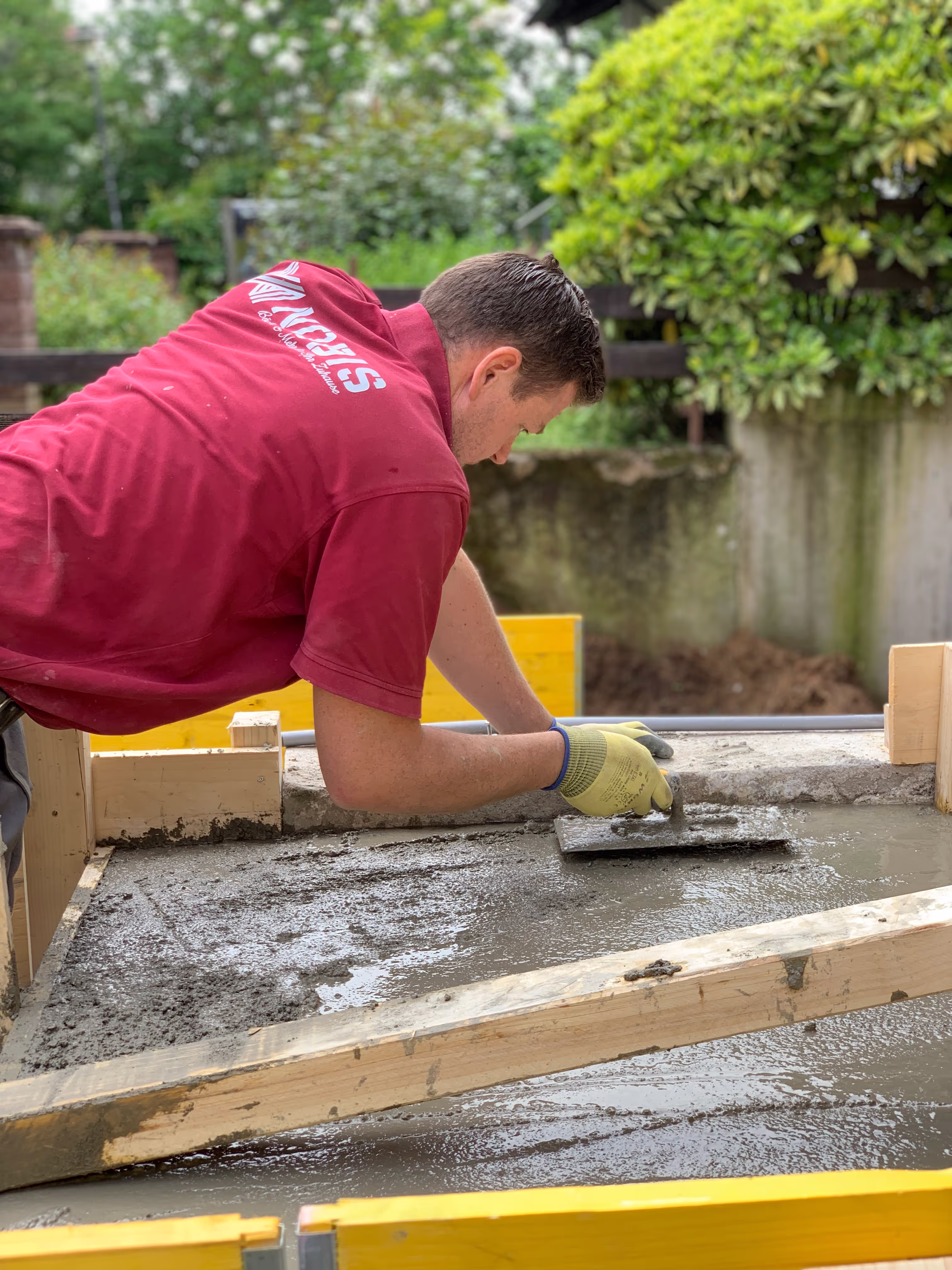 Mitarbeiter der Mehr-Bau GmbH glättet frischen Beton in einer Holzschalung im Garten