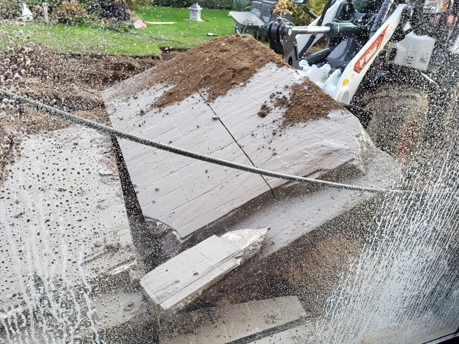 Baggerschaufel hebt ein getrenntes Stück Betonplatte an, Wasser spritzt
