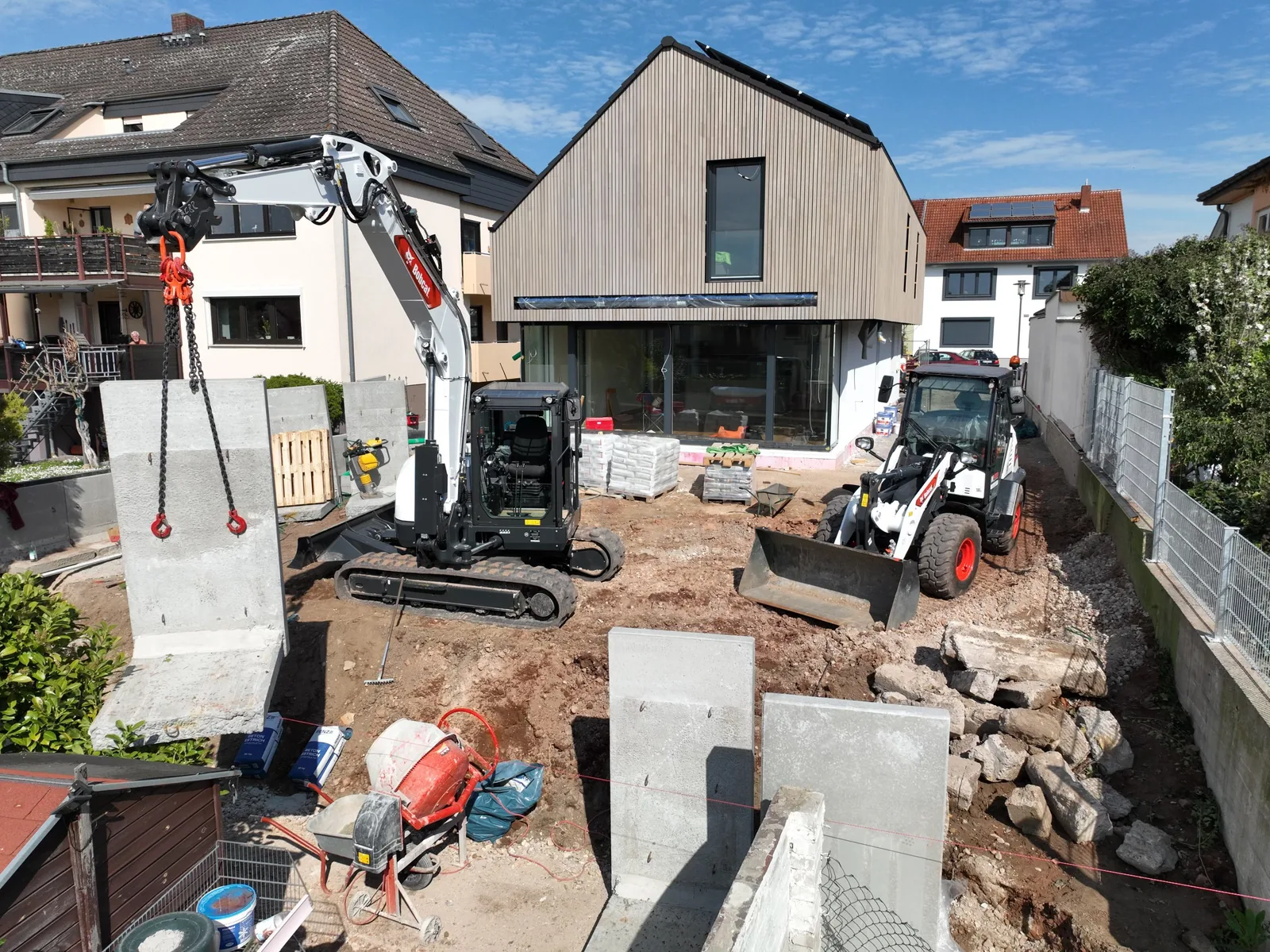 Baustelle der Mehr-Bau GmbH: Minibagger und Radlader vor einem neu mit Holz verkleideten Wohnhaus