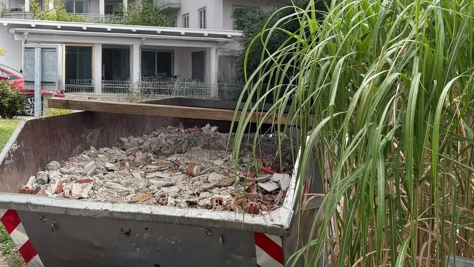 Absetzcontainer im Garten, gefüllt mit gemischtem Bauschutt aus Ziegeln, Fliesen und Putz