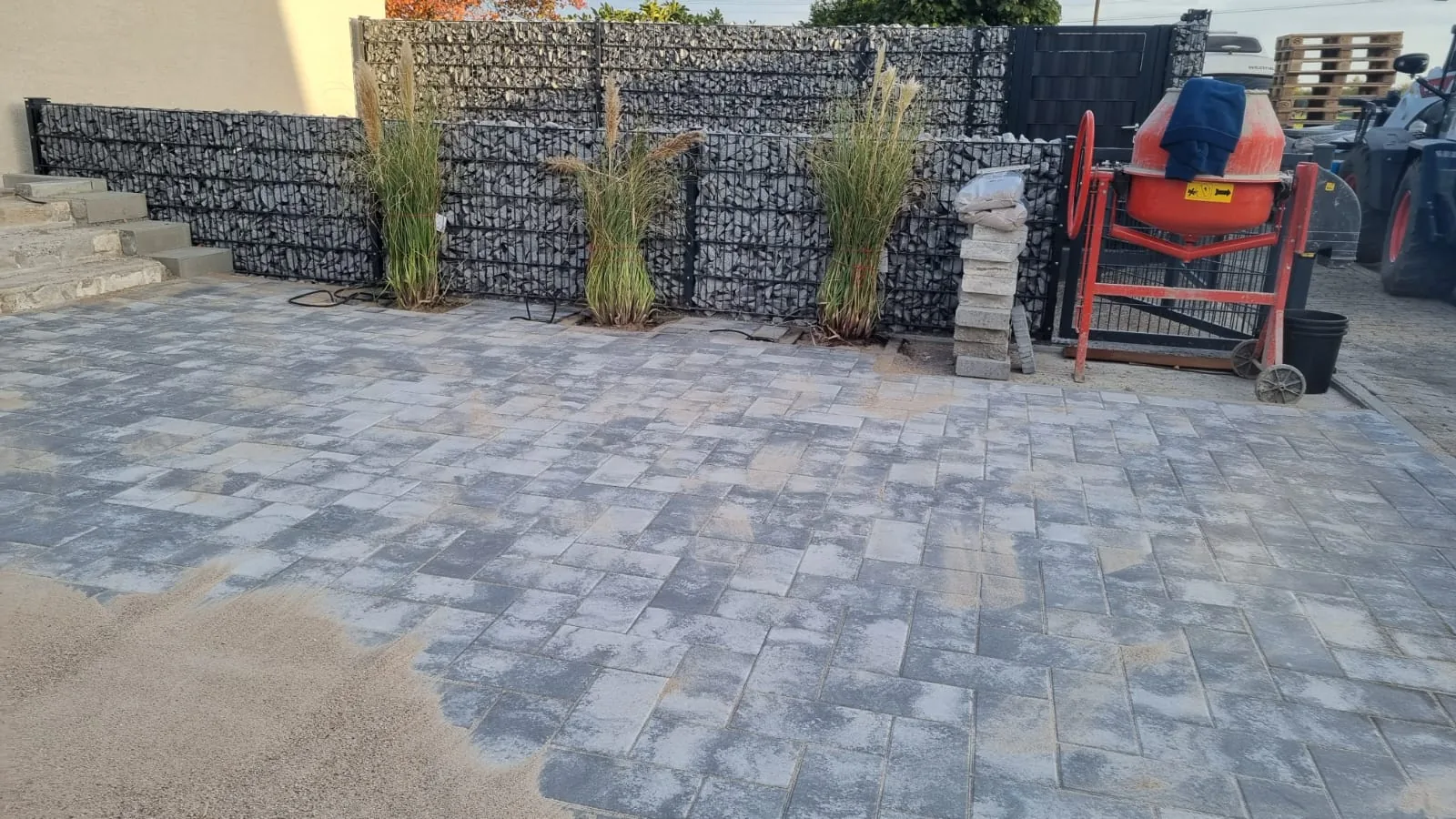 Gabionenwand mit Ziergräsern davor und angrenzender Pflasterfläche