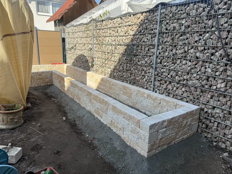 Fertig gesetztes Naturstein-Hochbeet vor einer Gabionenwand mit Sichtschutz
