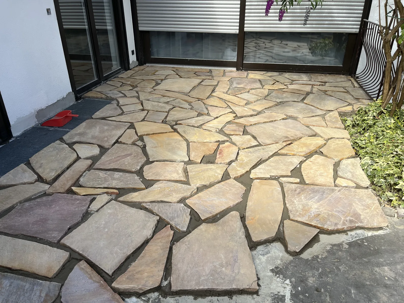 Fertige Natursteinterrasse aus Polygonalplatten vor einem weißen Wohnhaus