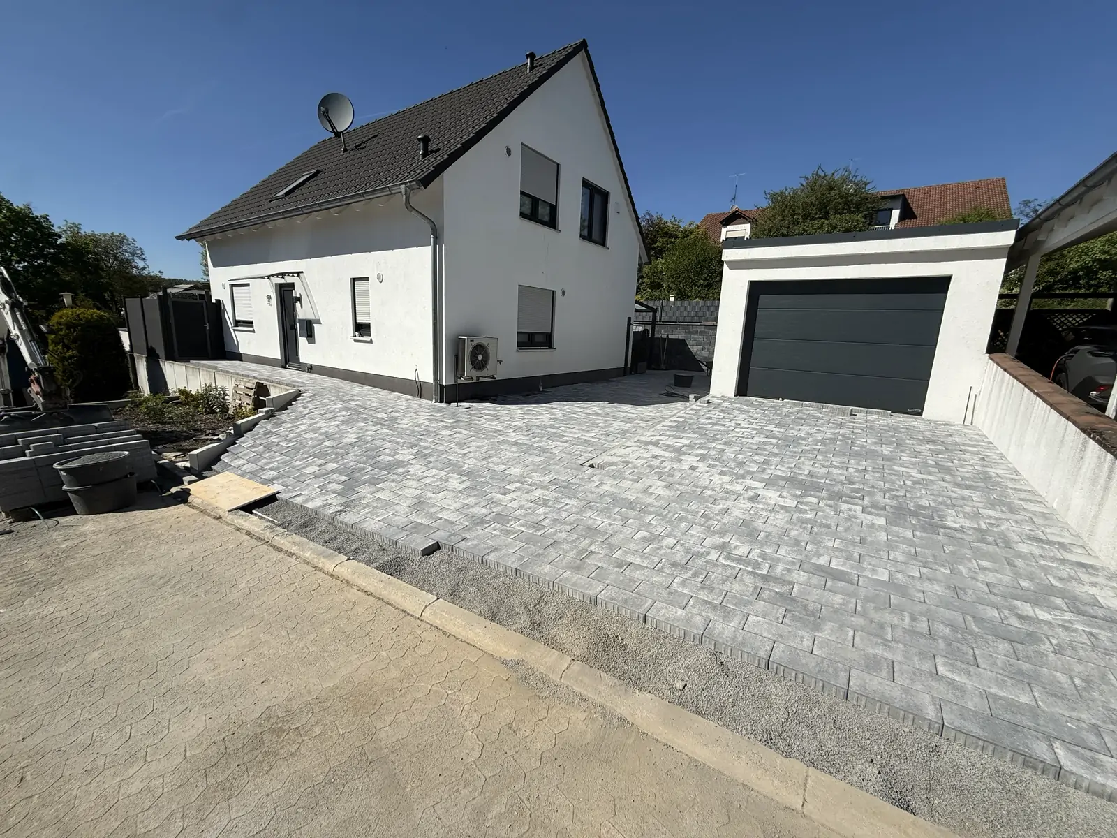 Fertig gepflasterte Hofeinfahrt vor einem weißen Wohnhaus mit dunkler Garage
