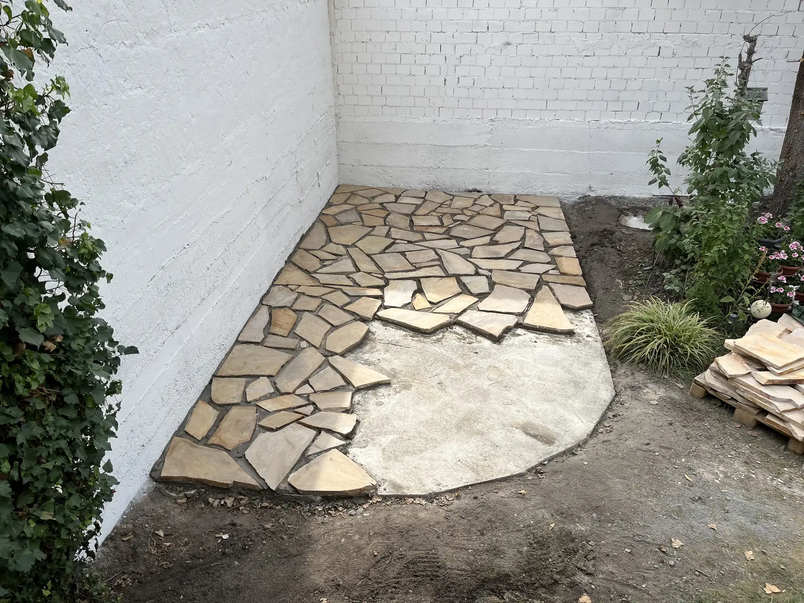Halb verlegte Polygonalplatten aus Sandstein, weitere Platten auf Paletten daneben