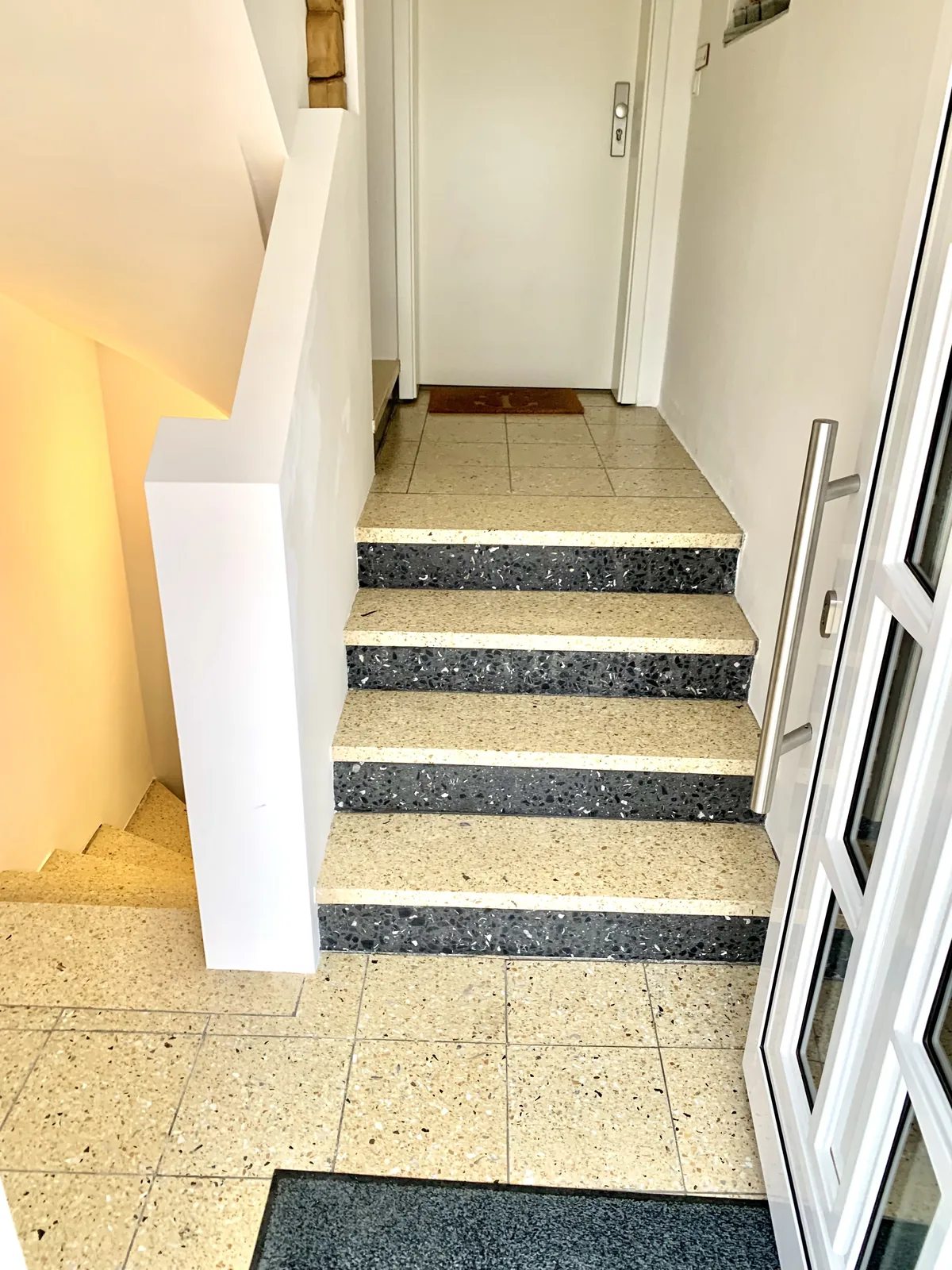 Eingangsbereich mit hellem Terrazzoboden und dunkel abgesetzten Treppenstufen