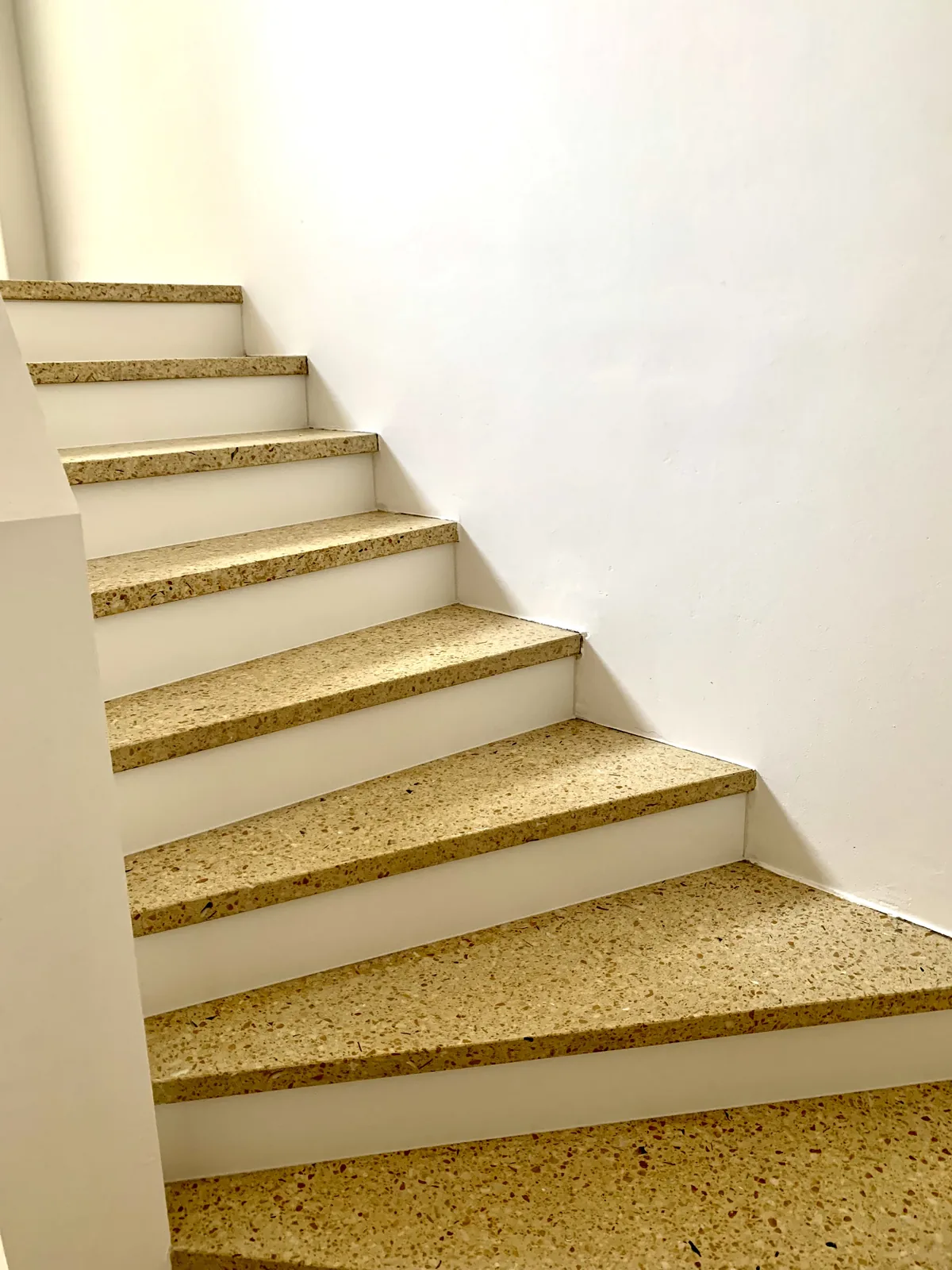 Treppenlauf mit hellen Terrazzostufen vor weißer Wand