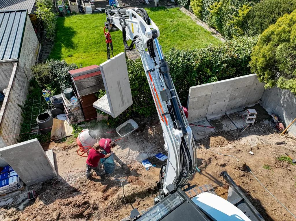 Arbeiter richten ein gesetztes Betonfertigteil der Stützwand aus