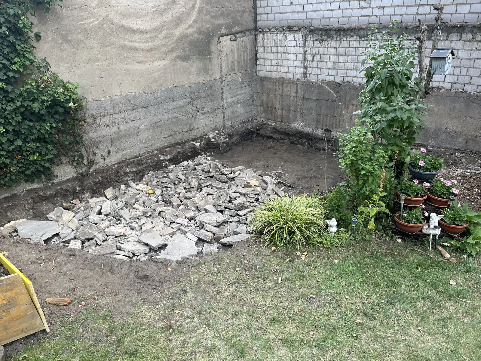 Gartenecke im Rückbau: gebrochene Platten aufgestapelt, Erdboden freigelegt