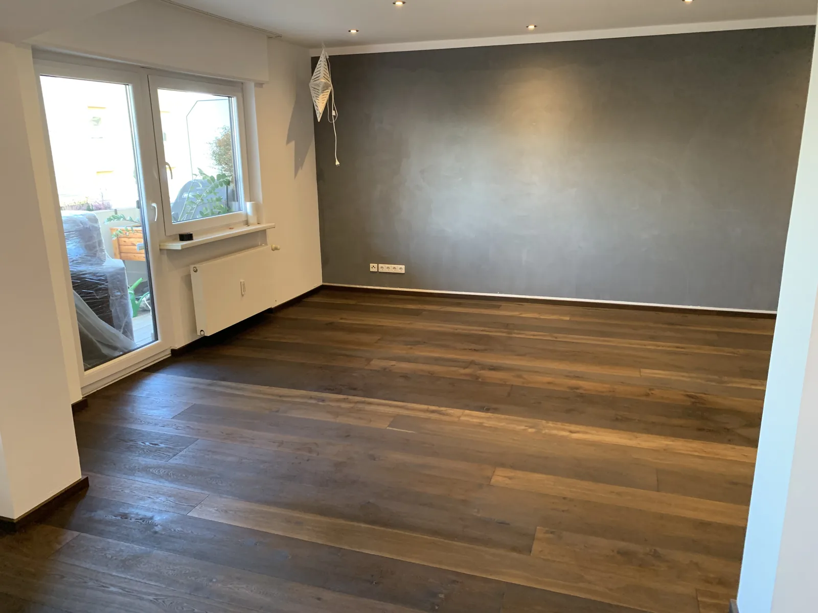 Große grau gespachtelte Wand in einem Wohnraum mit dunklem Parkett