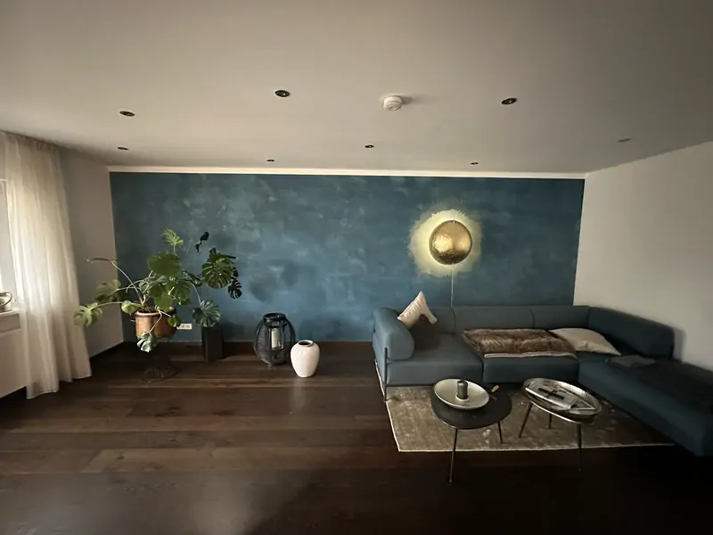 Wohnzimmer mit petrolblau lasierter Wand, dunklem Massivholzparkett und Wandleuchte